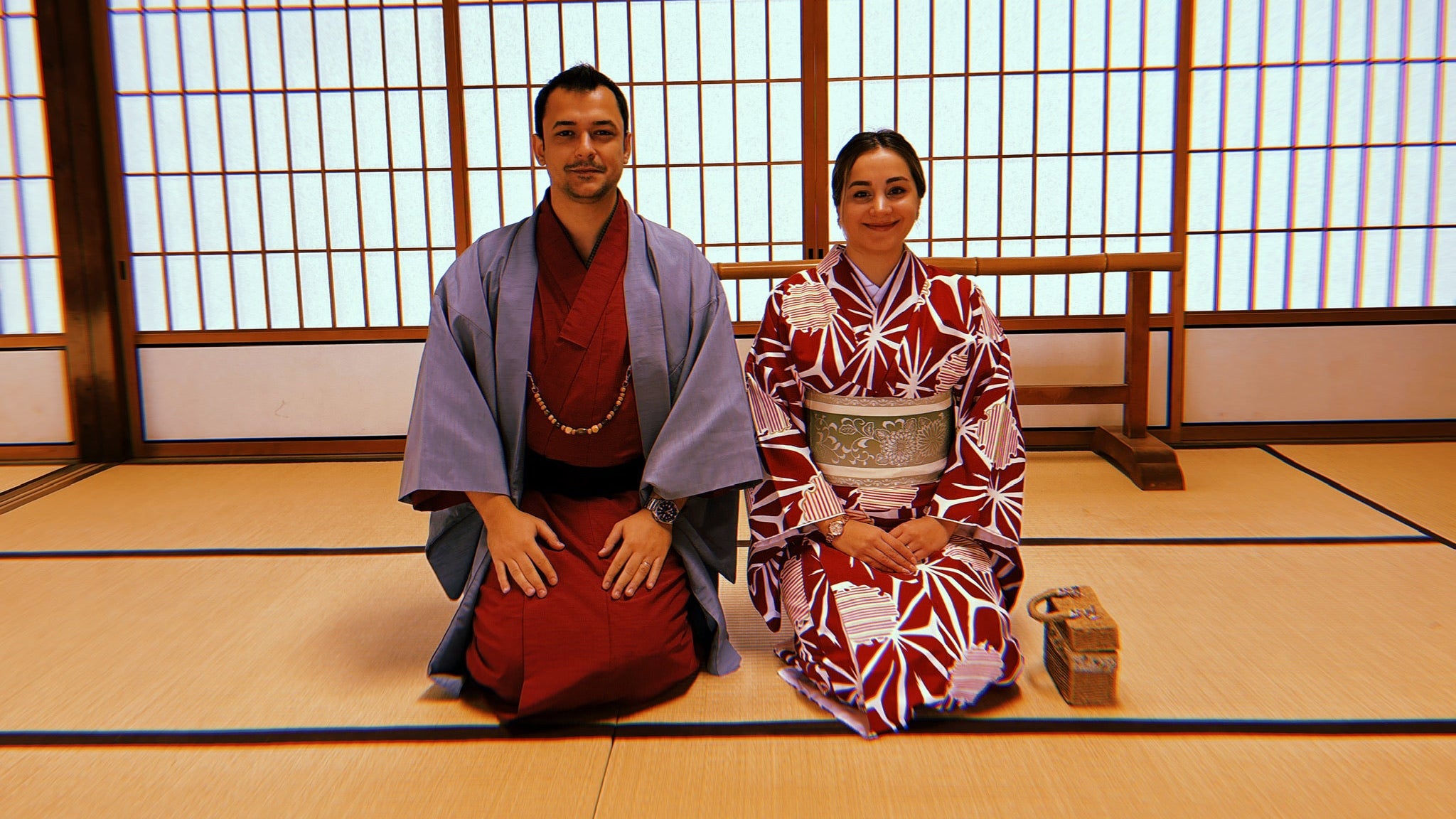 Two people in traditional Japanese attire sitting on the floor in a room with shoji screens.